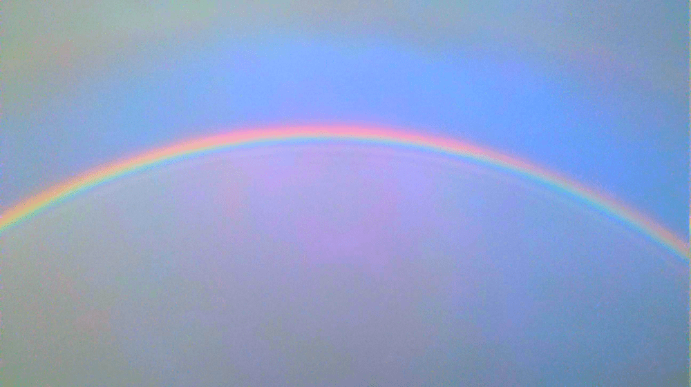 the arc of a full rainbow in a summer sky